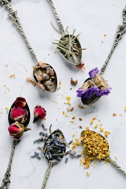 Aesthetic flat lay of vintage spoons filled with various dried herbs and flowers on a marble surface.